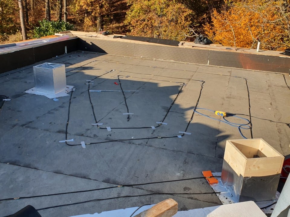 Sensorbasiertes Feuchtigkeits-Monitoring auf Flachdach — schwarze Sensorkabel mit weißen Befestigungsclips auf Bitumenbahn