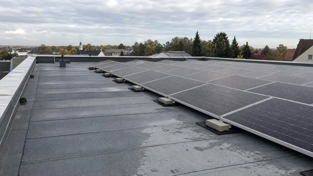 PV-Anlage auf einem europäischen Flachdach ohne sichtbare Dachdurchdringung mit Wartungsweg und Attika